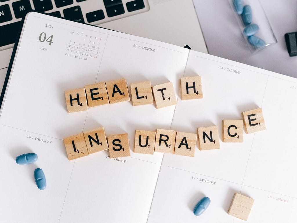 Imagine of wooden tiles spelling out "health insurance" sitting on top of a planner with white pages that someone uses to schedule their online counseling in Toronto