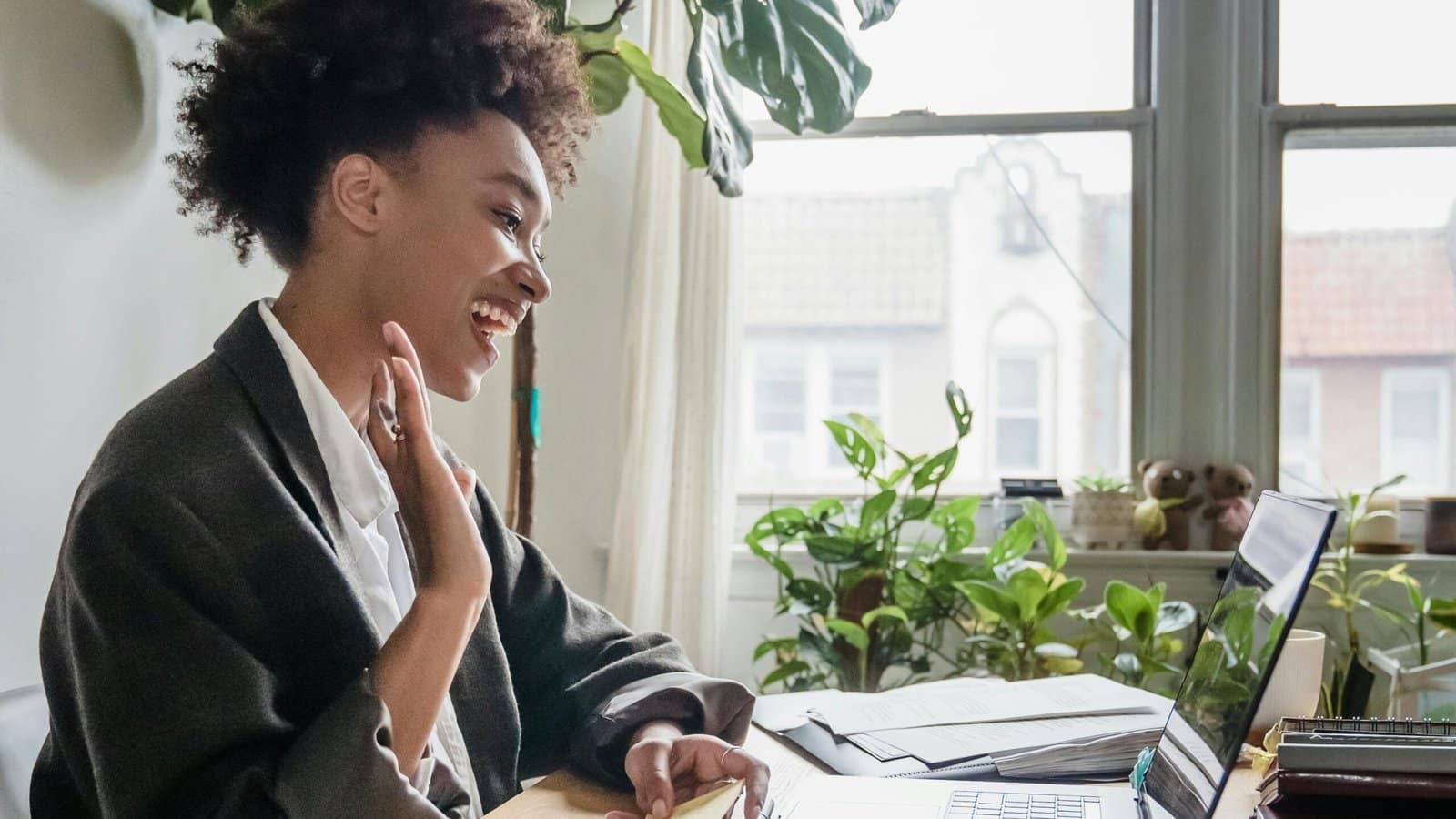 A woman sitting in her home office and smiling and waving at her computer as she does online counseling in Ontario