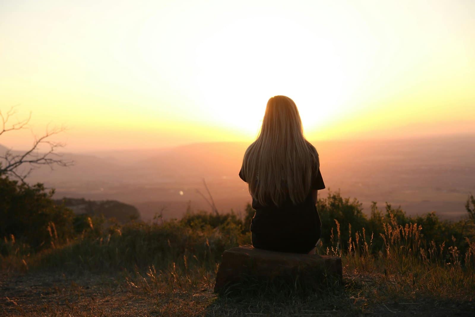 Sad woman sitting alone outside and staring at a sunset as she struggles with her depression symptoms