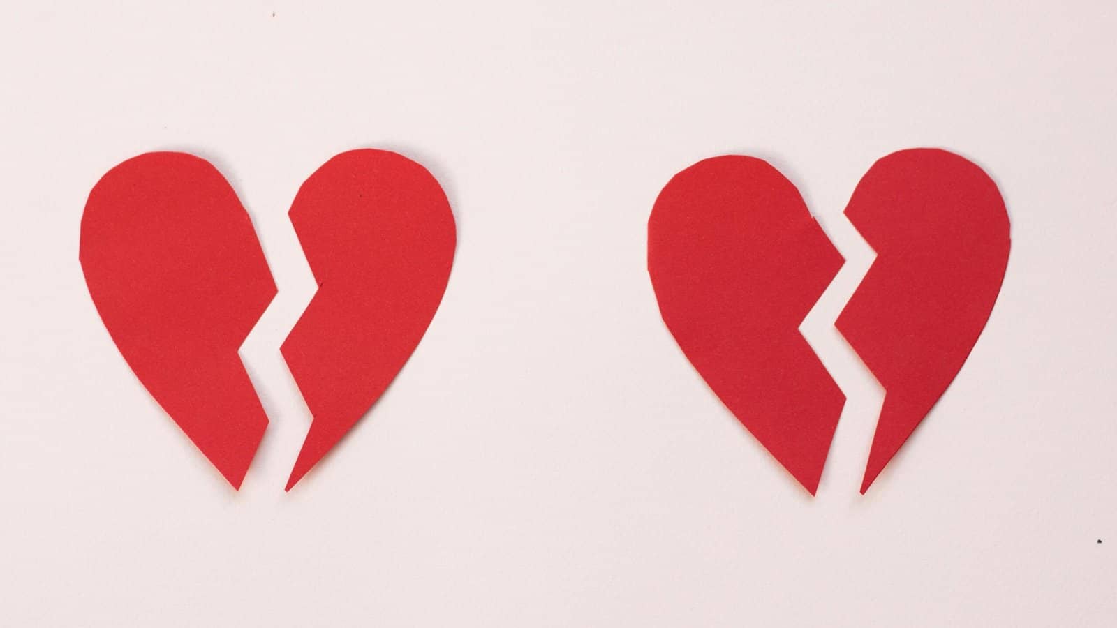 Two red broken hearts made out of construction paper sitting on a pale pink table symbolizing how to get over a breakup