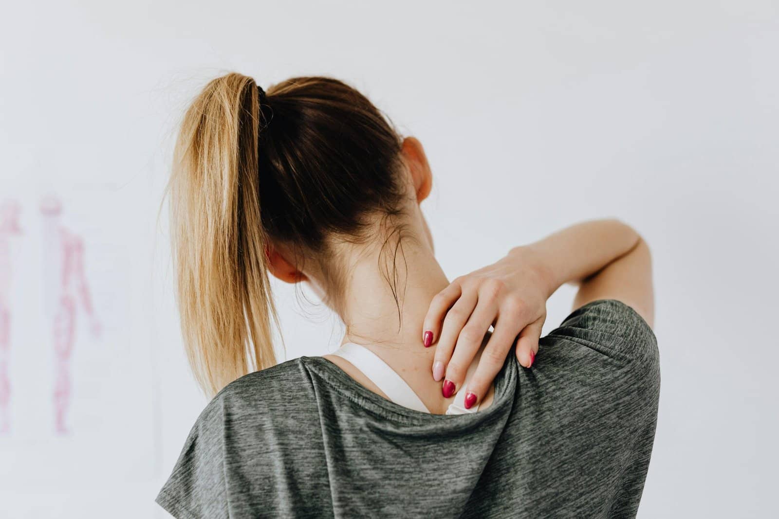 A woman struggling with chronic pain and depression facing away from the camera and holding her hand to her sore upper back.